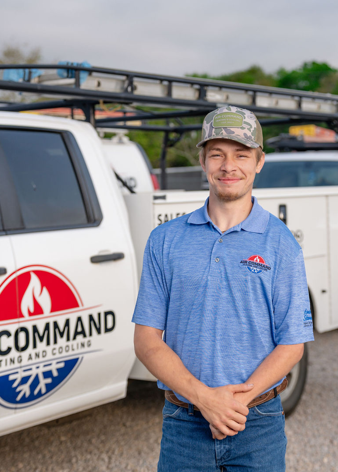 Jorage C., Installation Crew Member at Air Command Heating and Cooling, smiling in front of company service trucks in Hartford, AL.