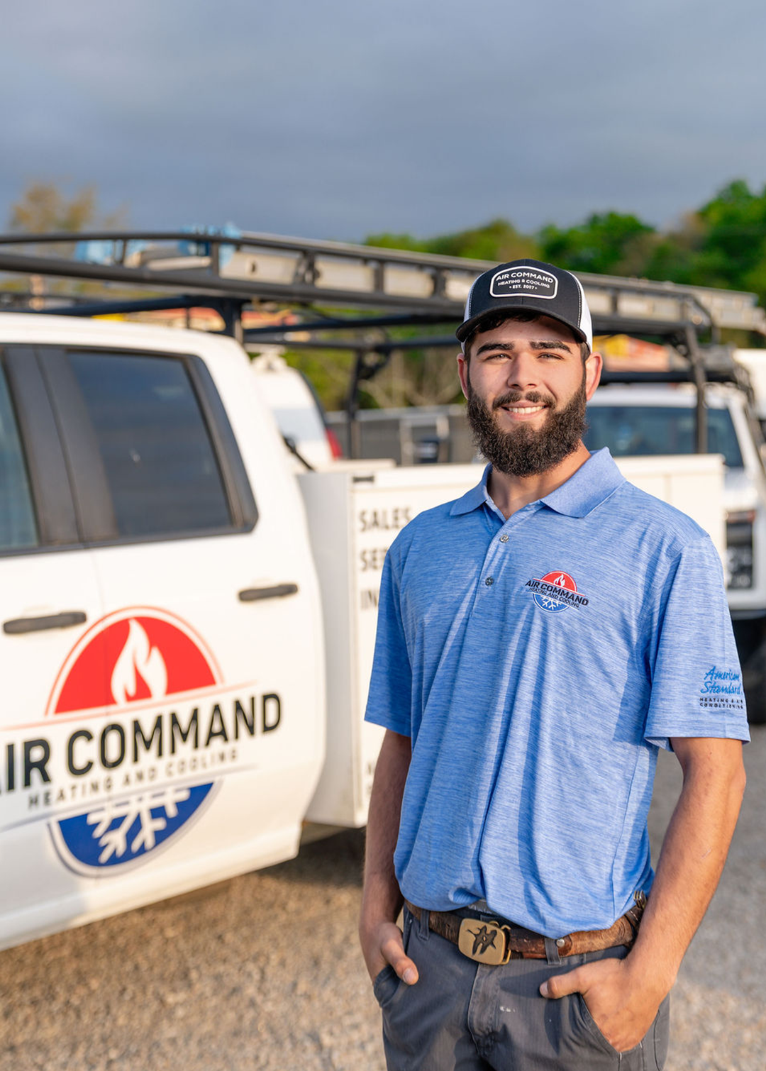Noah Owens, Installation Crew Member at Air Command Heating and Cooling, smiling in front of company service trucks in Hartford, AL.